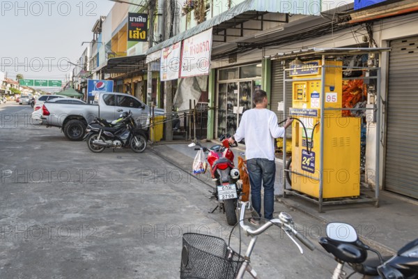 Thai man filling motor scooter with gasoline from a remote Sun Oil pump in Chiang Rai, Thailand