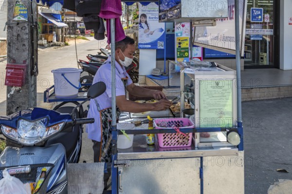 Thai man preparing food at his sidewalk food cart in Chiang Rai province of Northern Thailand