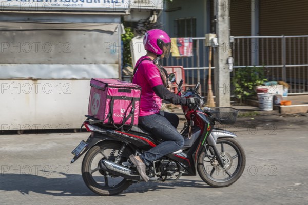 Food delivery drivers and other Thai motor scooter riders at a traffic light in Chiang Rai, Thailand