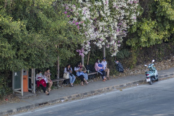 Thai women on cell phone while waiting for bus at bus stop in Chiang Rai, Thailand