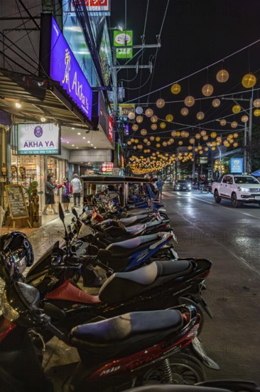 Motor scooters line the side of the downtown street in Chiang Rai, Thailand