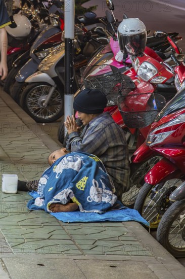 Homeless woman and son begging for money on the downtown street at night in Chiang Rai, Thailand