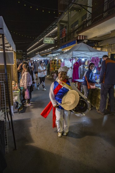 Cheery Thai woman beating a drum as she dances through the Night Market in downtown Chiang Rai, Thailand