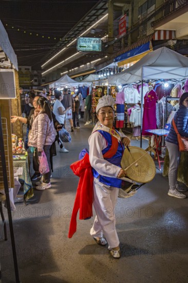 Smiling Thai woman beating a drum as she dances through the Night Market in downtown Chiang Rai, Thailand