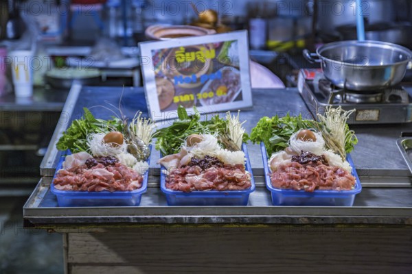 Thai street vendor offers hot pot meal package for customer to cook on a hot pot at their table at the night market in downtown Chiang Rai, Thailand