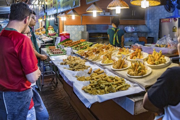 Customers looking over choices of fresh fried seafood at the night market in downtown Chiang Rai, Thailand