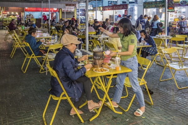 Thai mother and daughter preparing a meal in a hot pot at their table at the night market in downtown Chiang Rai, Thailand