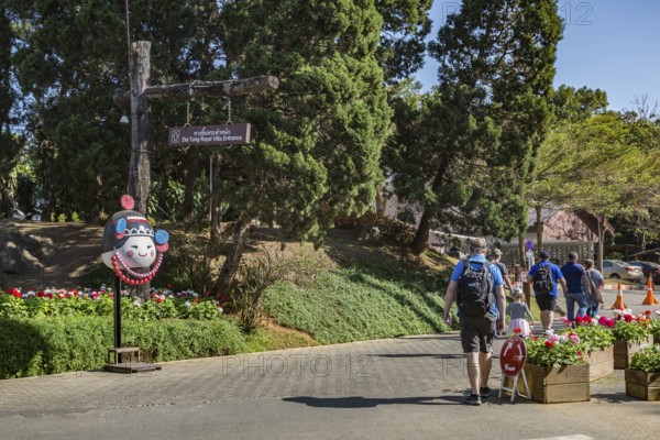 American tourists walking past a sign pointing to the entrance to the Doi Tung Royal Villa inside the Doi Tung tourist attraction in Chiang Rai, Thailand