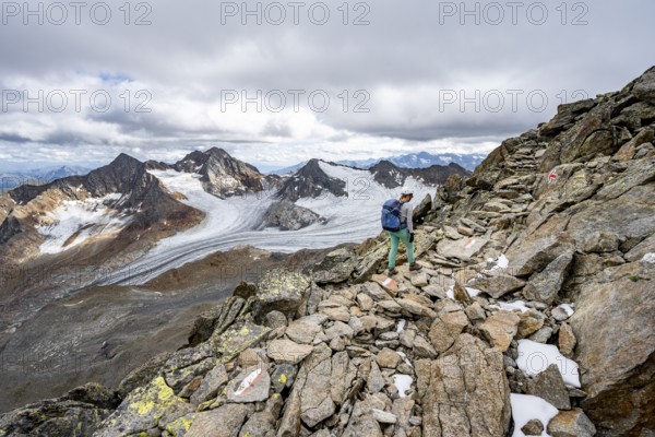 Mountaineer with helmet on a rocky hiking trail, in high mountain landscape, view of blue glacial lakes, mountain peaks Königshofspitz and Hofmannspitze with glacier of the Übeltalferner, Stubai Alps, South Tyrol, Italy