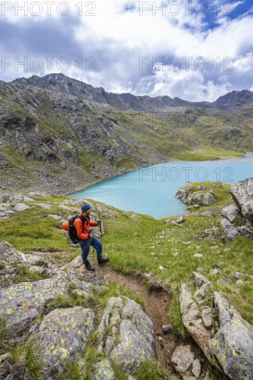 Mountaineers on a hiking trail, view of light blue mountain lake Trüber See in barren mountain landscape, Seven Lakes Hike, Stubai Alps, near Ridnaun, South Tyrol, Italy