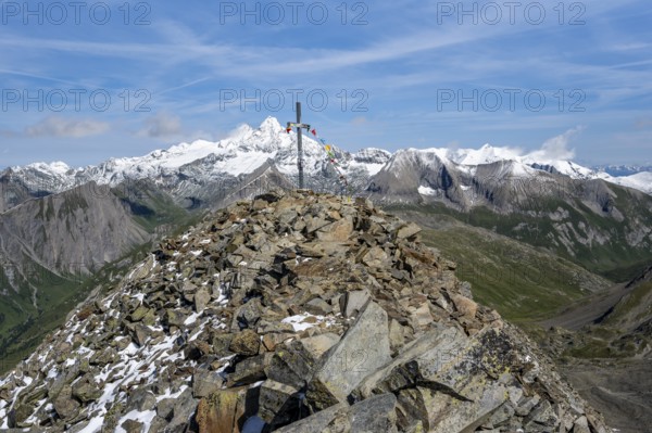 Böses Weibl summit with summit cross and colourful prayer flags, view of picturesque mountain landscape with snow-covered summit of the Großglockner, Wiener Höhenweg, Schober group, Hohe Tauern National Park, Carinthia, Austria