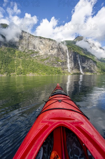 Kayak trip on the Geirangerfjord with waterfall The Seven Sisters, tip of a red kayak in the fjord, atmospheric fjord landscape with reflection, first person view, near Geiranger, Møre og Romsdal, Norway