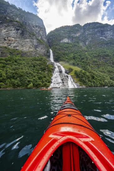 Kayak trip on the Geirangerfjord at the Freier waterfall, tip of a red kayak in the fjord, atmospheric fjord landscape, first person view, near Geiranger, Møre og Romsdal, Norway