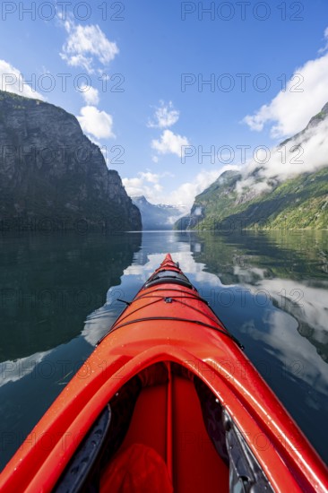 Kayak trip on the Geirangerfjord, tip of a red kayak in the fjord with reflection, atmospheric fjord landscape, first person view at Geiranger, Møre og Romsdal, Norway