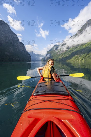 Kayak trip on the Geirangerfjord, young woman paddling in a red kayak, atmospheric fjord landscape, Møre og Romsdal, Norway