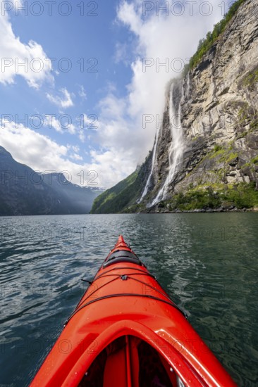Kayak trip on the Geirangerfjord at the waterfall The Seven Sisters, tip of a red kayak in the fjord, atmospheric fjord landscape, first person view, near Geiranger, Møre og Romsdal, Norway