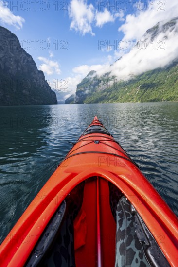 Kayak trip on the Geirangerfjord, tip of a red kayak in the fjord with reflection, atmospheric fjord landscape, first person view at Geiranger, Møre og Romsdal, Norway