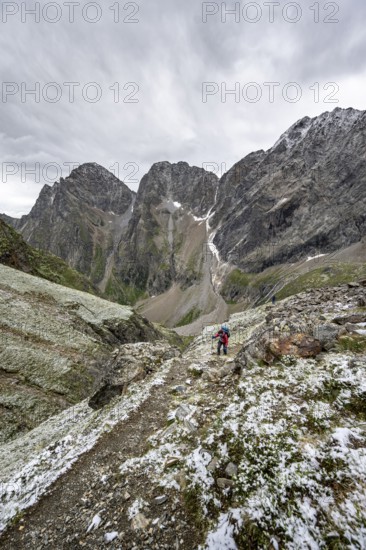 Mountaineer on hiking trail in steep rocky mountain landscape with fresh snow in summer, behind mountain peaks Großer Friedrichskopf and Georgskopf, ascent to Hornscharte, Schober group, Hohe Tauern National Park, Carinthia, Austria