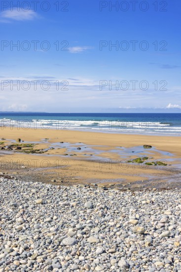 Pebble beach by the sea with a seascape view to the horizon and breaking waves on the shore a sunny summer day with a blue sky, Crozon peninsula, Bretagne, France