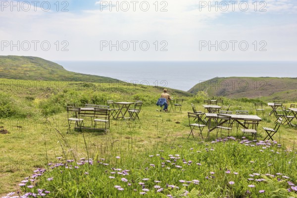 Outdoor cafe with a alone woman sitting by a table on a meadow with a sea view in the summer, Crozon peninsula, Bretagne, France