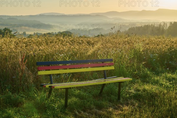 Bench in national colours with peaceful view of misty fields in the morning light, Germerode, Geo nature park Park Frau-Holle-Land, Hoher Meissner, Hesse, Germany