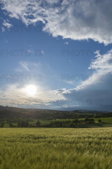 Dramatic cloudy sky with approaching storm and last sunbeams, Frankenhain, dark cloud wall, thunderstorm in lift, cumulus clouds, sunbeams, low mountain range landscape, agriculture, forest, grain field, backlight shot, municipality Berkatal, Werra-Meissner-Kreis, Hesse, Germany