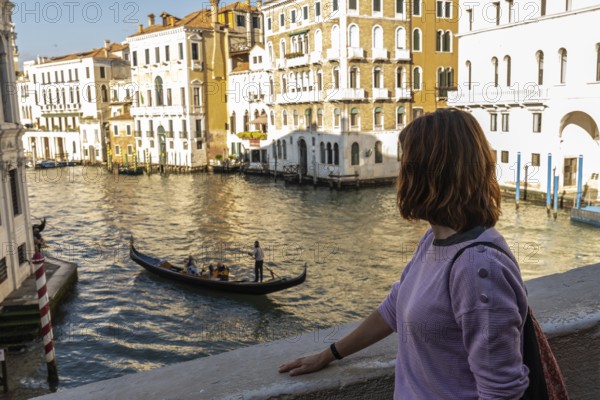 Young woman enjoying picturesque view of traditional gondola sailing on grand canal amidst historic venetian buildings