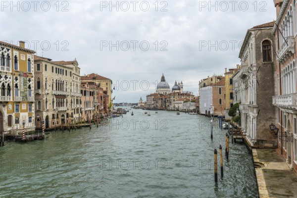 Scenic view of the grand canal flowing through venice, showcasing colorful historic buildings and the majestic basilica di santa maria della salute under a cloudy sky