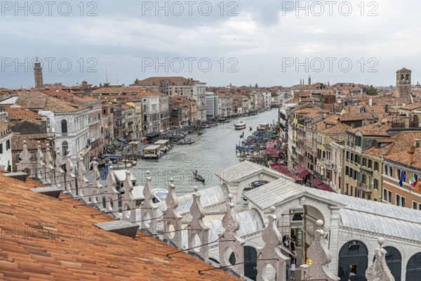 Gondolas navigating the grand canal amidst historic buildings in venice, italy, seen from a rooftop with terracotta tiles