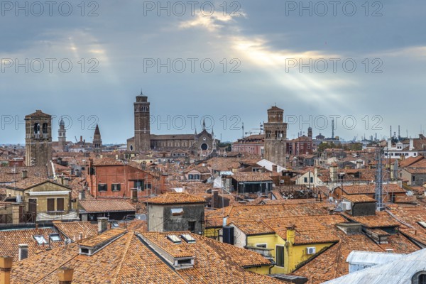 Stunning cityscape of venice with terracotta rooftops, churches, and sun rays piercing through clouds