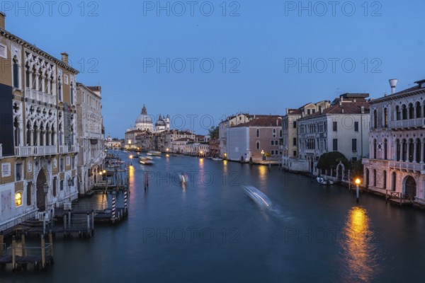 Motorboats creating motion blur are navigating grand canal with basilica di santa maria della salute in background at blue hour