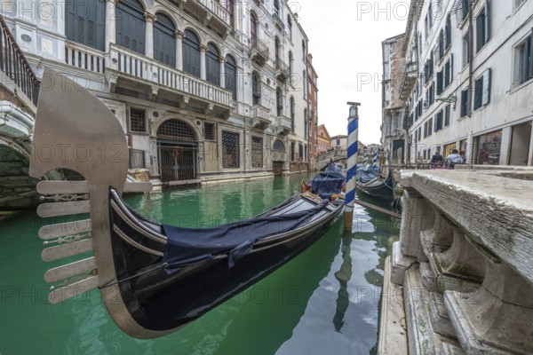Traditional gondola moored in venice canal with turquoise water, near a bridge and old buildings, showing venetian architecture and lifestyle