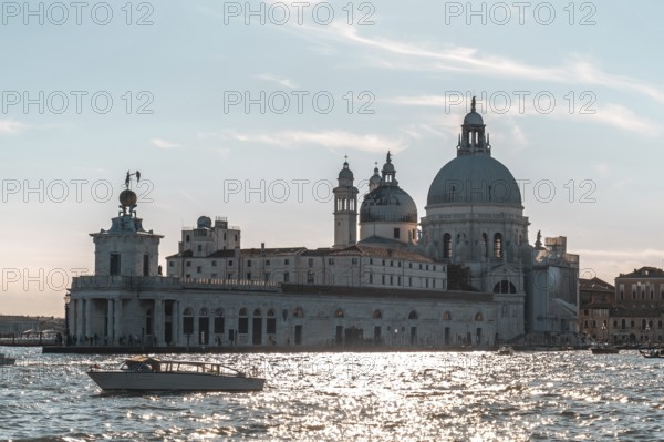 Motorboat navigating grand canal with punta della dogana and basilica di santa maria della salute reflecting on water surface at sunset in venice, italy