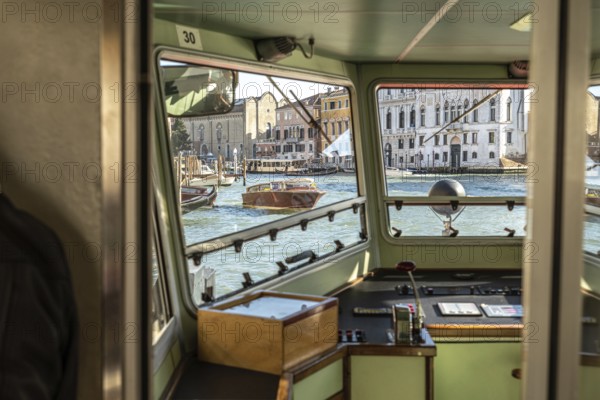 View from inside a vaporetto cockpit navigating grand canal in venice, with traditional venetian buildings and boats in the background