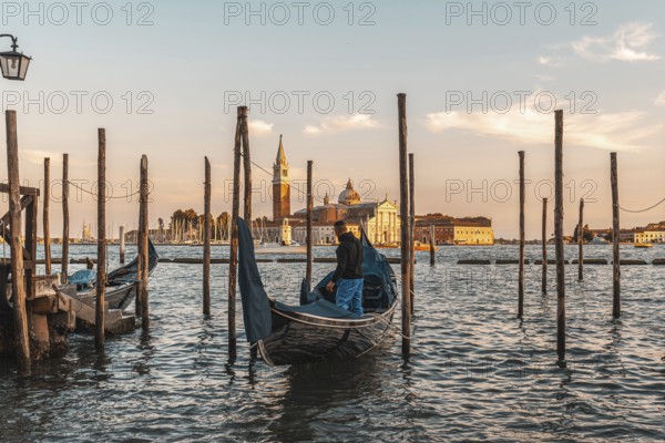 Gondolier preparing his gondola in venice, italy, at sunset, with the church of san giorgio maggiore in the background
