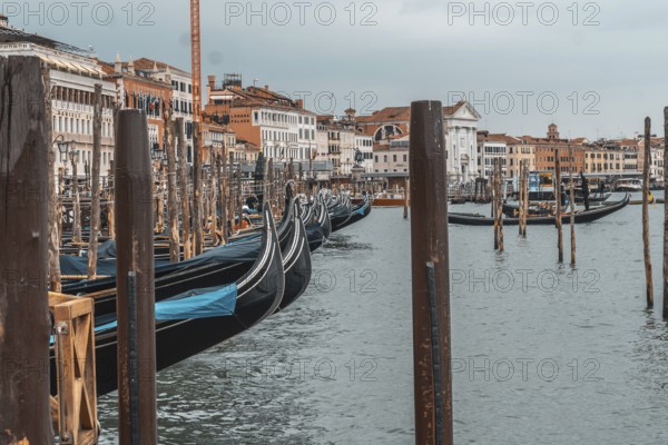 Gondolas moored near the rialto bridge in venice, waiting patiently for tourists on a cloudy day, create a serene and picturesque scene