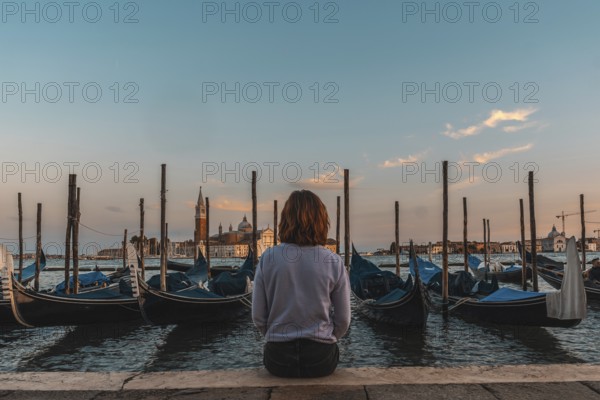 Young woman enjoying the sunset over the venetian lagoon with gondolas moored in the foreground and the san giorgio maggiore church in the background