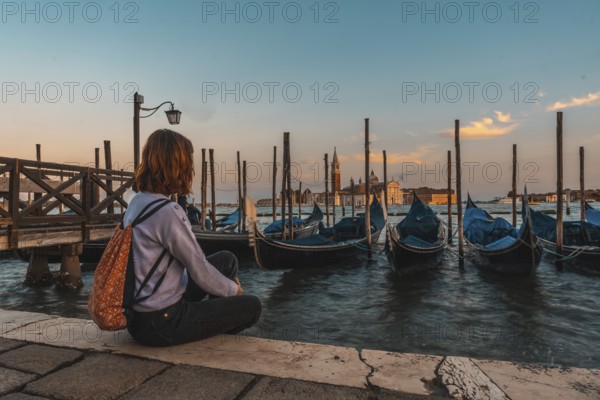 Young woman admiring gondolas and san giorgio maggiore church in venice, italy, during a beautiful sunset