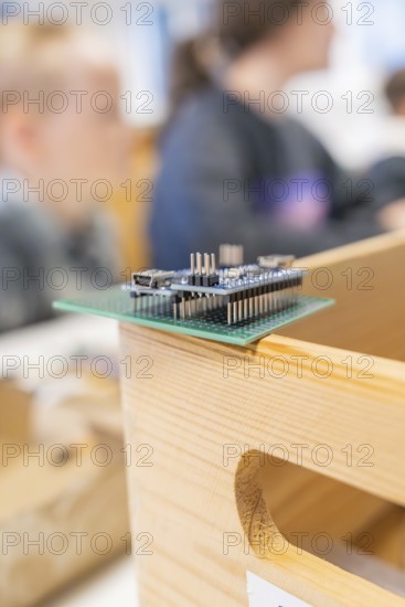 Technological circuit board on a wooden box with blurred people in the background, Nagold Youth Research Centre, Germany