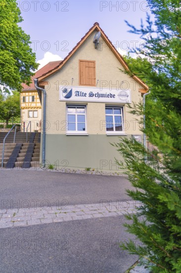 Small traditional building with sign, surrounded by trees and road, Deufringen, Aidlingen, Germany