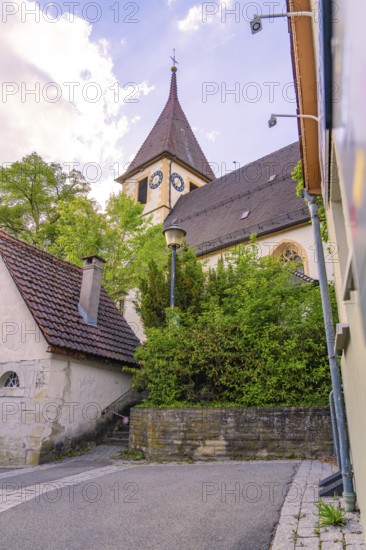 Gothic church with clock tower and surrounding trees, next to a wall, Deufringen, Aidlingen, Germany