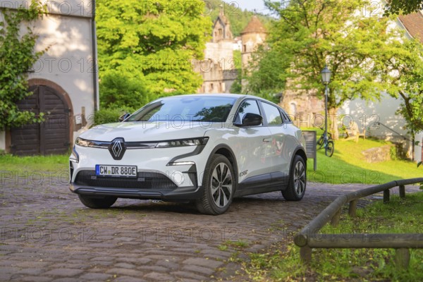 White car parked on a cobbled path in front of old buildings and a green summer backdrop, Renault Megane, Deer E Carsharing, electric car, Calw, Black Forest, Germany