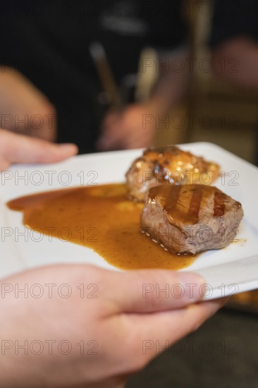 Hand holding a plate with two pieces of roasted meat and plenty of sauce in a kitchen, event and wedding location Kloster Lorch, Lorch, Germany