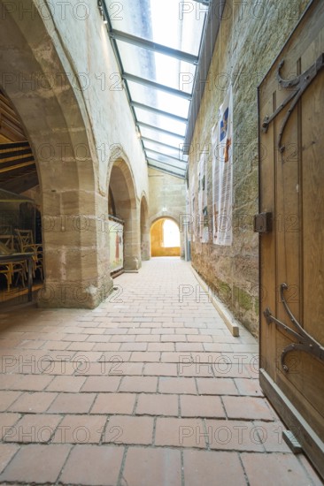 Corridor with medieval architecture, wooden chairs and wooden door, flooded with sunlight, event and wedding location Lorch Monastery, Lorch, Germany