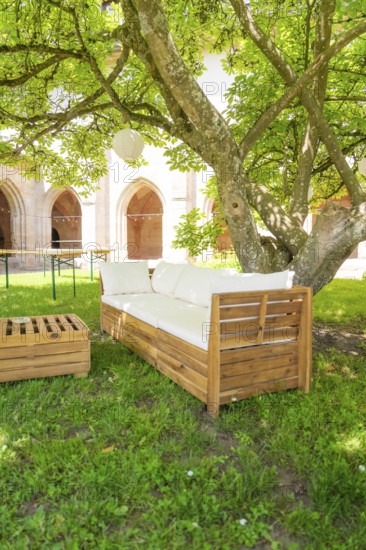 Wooden sofa under a tree in the garden with cushions, located in a shady forecourt, event and wedding location Kloster Lorch, Lorch, Germany