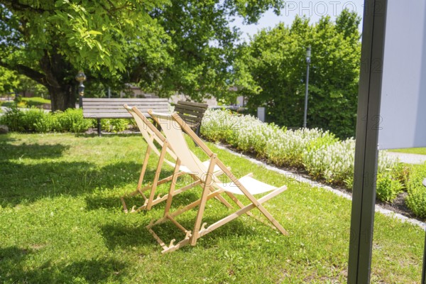 Two wooden deckchairs in the summer garden on a green lawn next to trees in the shade, event and wedding location Lorch Monastery, Lorch, Germany