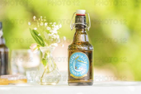 Bottle of Flensburger Strand beer on a table next to a vase of flowers in a green, natural setting, event and wedding location Kloster Lorch, Lorch, Germany