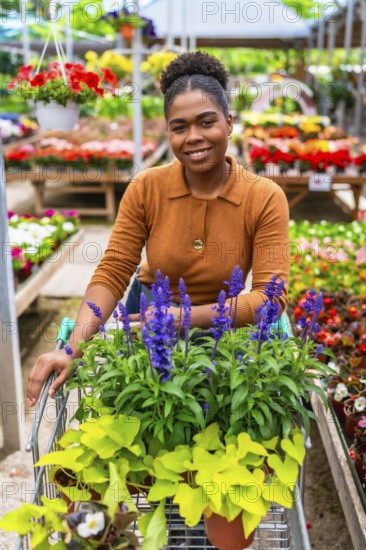 Happy young woman pushing a shopping cart, selecting vibrant flowers and plants while enjoying her time at a bustling garden center