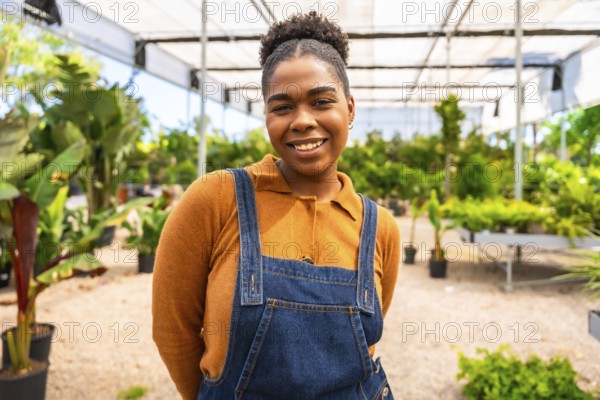 Portrait of a young african american woman smiling while working in a greenhouse, surrounded by vibrant plants and flowers