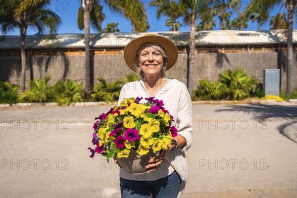 Happy gardener holding a pot of colorful petunias, enjoying a sunny day at the botanical garden